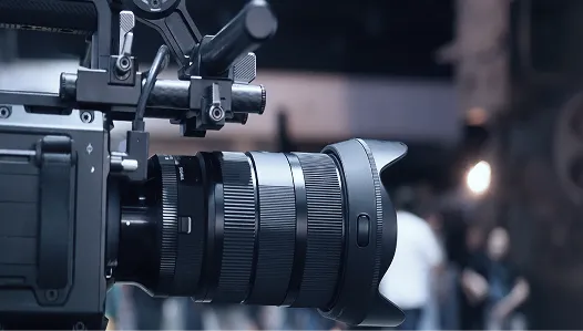 撮影スタジオと思われる場所でセットされた、黒い業務用ビデオカメラと大型レンズの側面